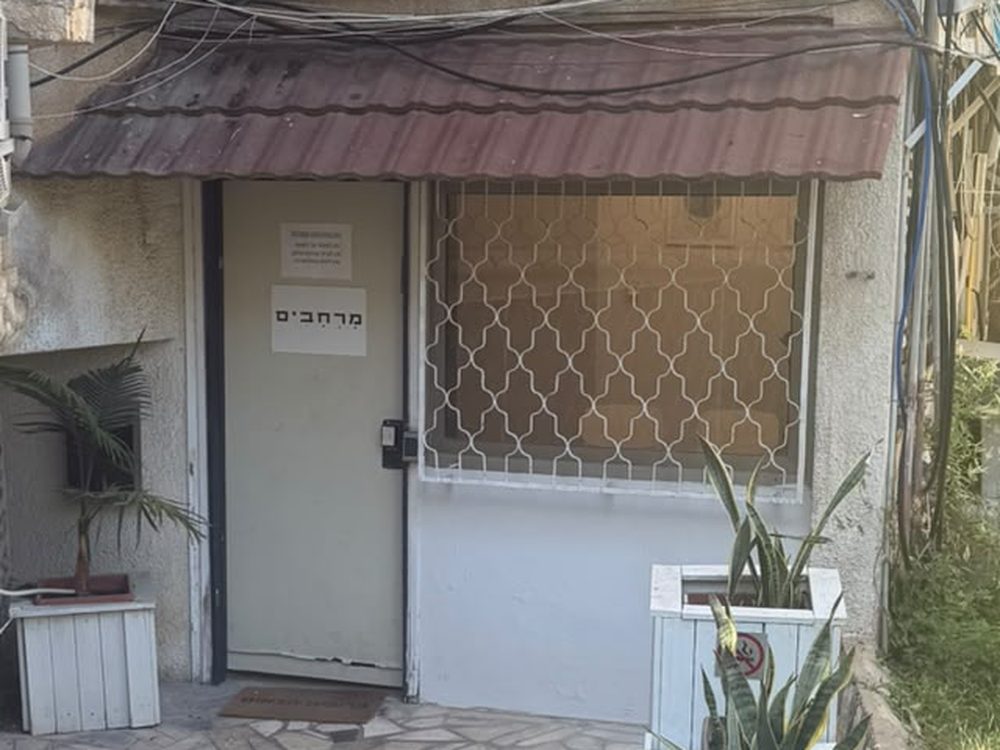 דלת הכניסה למרפאה, לבנה, עם שלט שעליו כתוב "מרחבים" וגגון רעפים מעליה.
